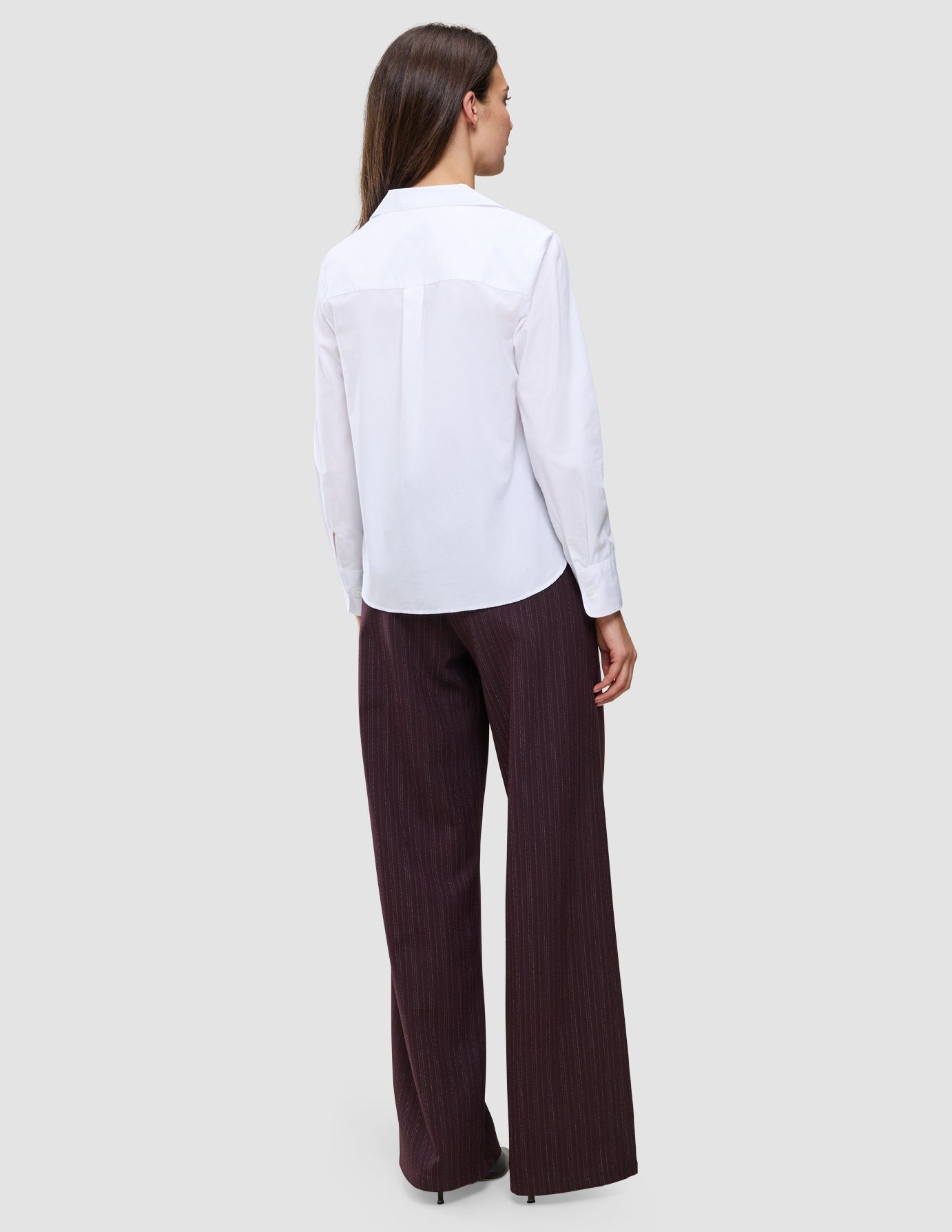 Eine Person, von hinten gesehen, die ein weißes Madison-Hemd und eine dunkle Nadelstreifenhose im klassischen, minimalistischen Stil trägt.